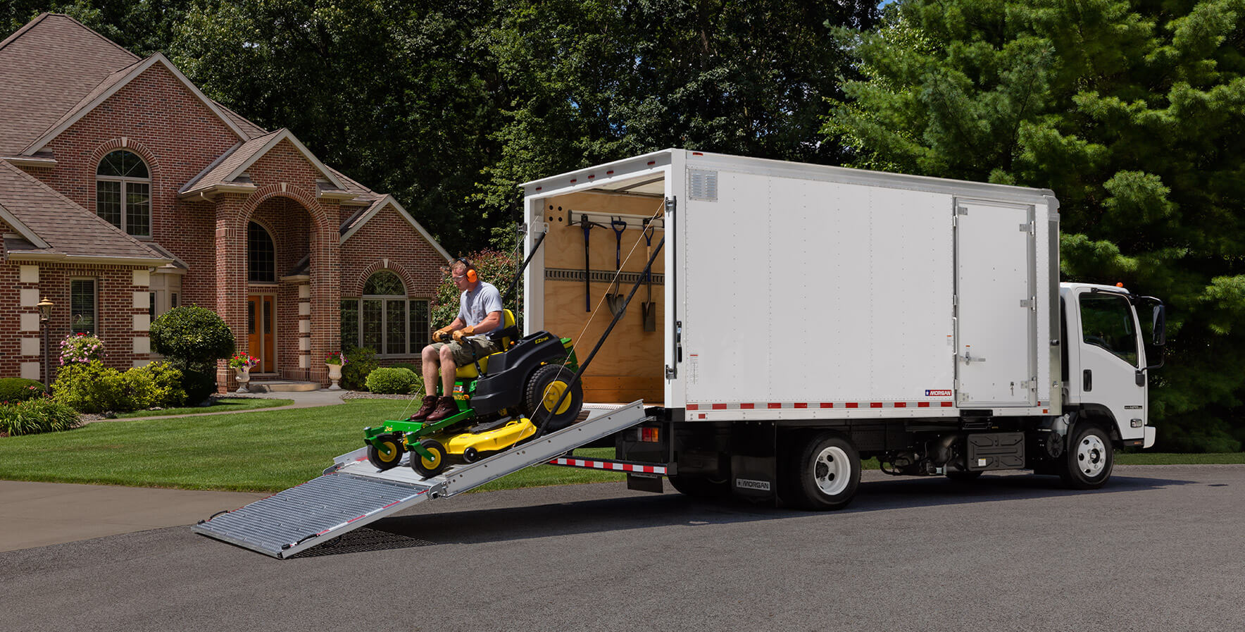 A landscaper driving a zero-turn mower out of the back of a Morgan ProScape box truck in Wake Forest, NC.